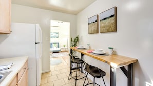 A compact kitchen with a refrigerator, a wooden dining table with chairs, and two framed pictures on the wall. - Quiet Carpinteria Cottage By Town & Beaches (Carpinteria)