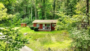 A small red cabin with a porch, surrounded by dense forest. - Maggie Valley Cottage Near Festival Grounds! (Maggie Valley)