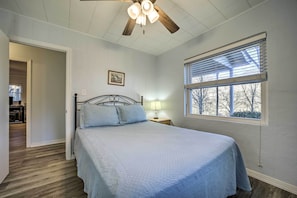 A bedroom with a bed, a ceiling fan, a window with blinds, and a door leading to another room.