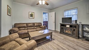 A living room with a brown leather sofa, a wooden coffee table, a fireplace, and a ceiling fan. - Maggie Valley Cottage Near Festival Grounds! (Maggie Valley)