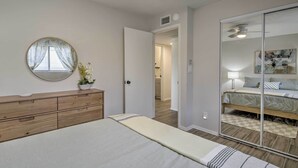 Een slaapkamer met een bed, een houten dressoir, een ronde spiegel en een schuifdeur naar een badkamer.