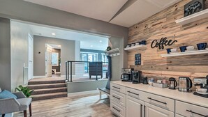 A modern kitchen with white cabinetry, a wooden accent wall with a 'Coffee' sign, and a staircase leading to a balcony. - Luxurious & Forested Oasis in Flagstaff w/ Hot Tub (Flagstaff)