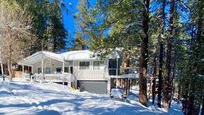 A two-story house with a covered porch and a garage, surrounded by snow-covered trees. - Luxurious & Forested Oasis in Flagstaff w/ Hot Tub (Flagstaff)