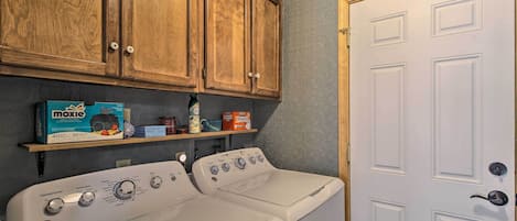 Un cuarto de lavandería con lavadora y secadora blancos, armarios de madera y una puerta.