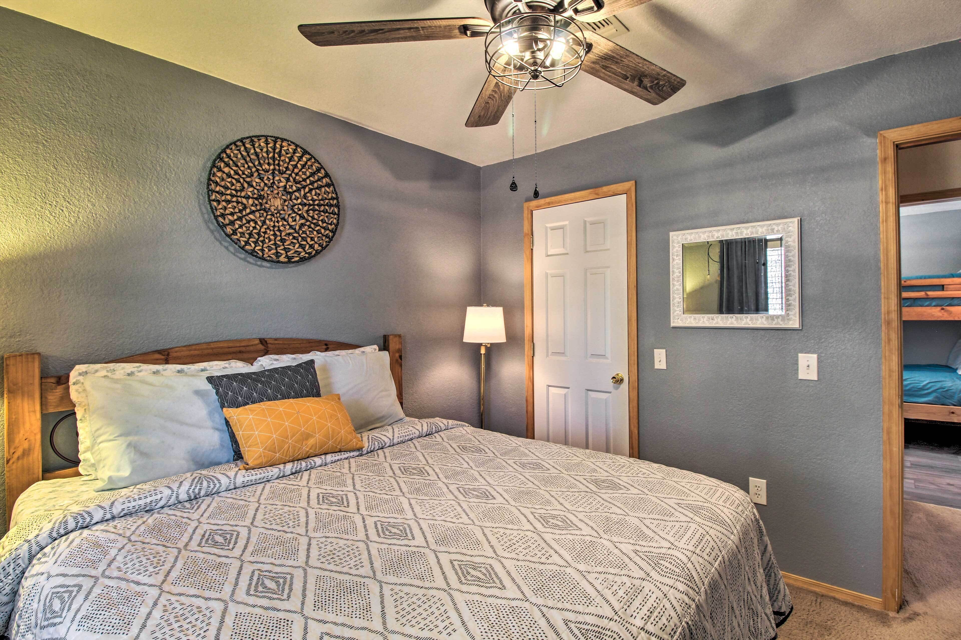 A bedroom with a bed, a ceiling fan, a door, a mirror, and a bunk bed in the adjacent room.