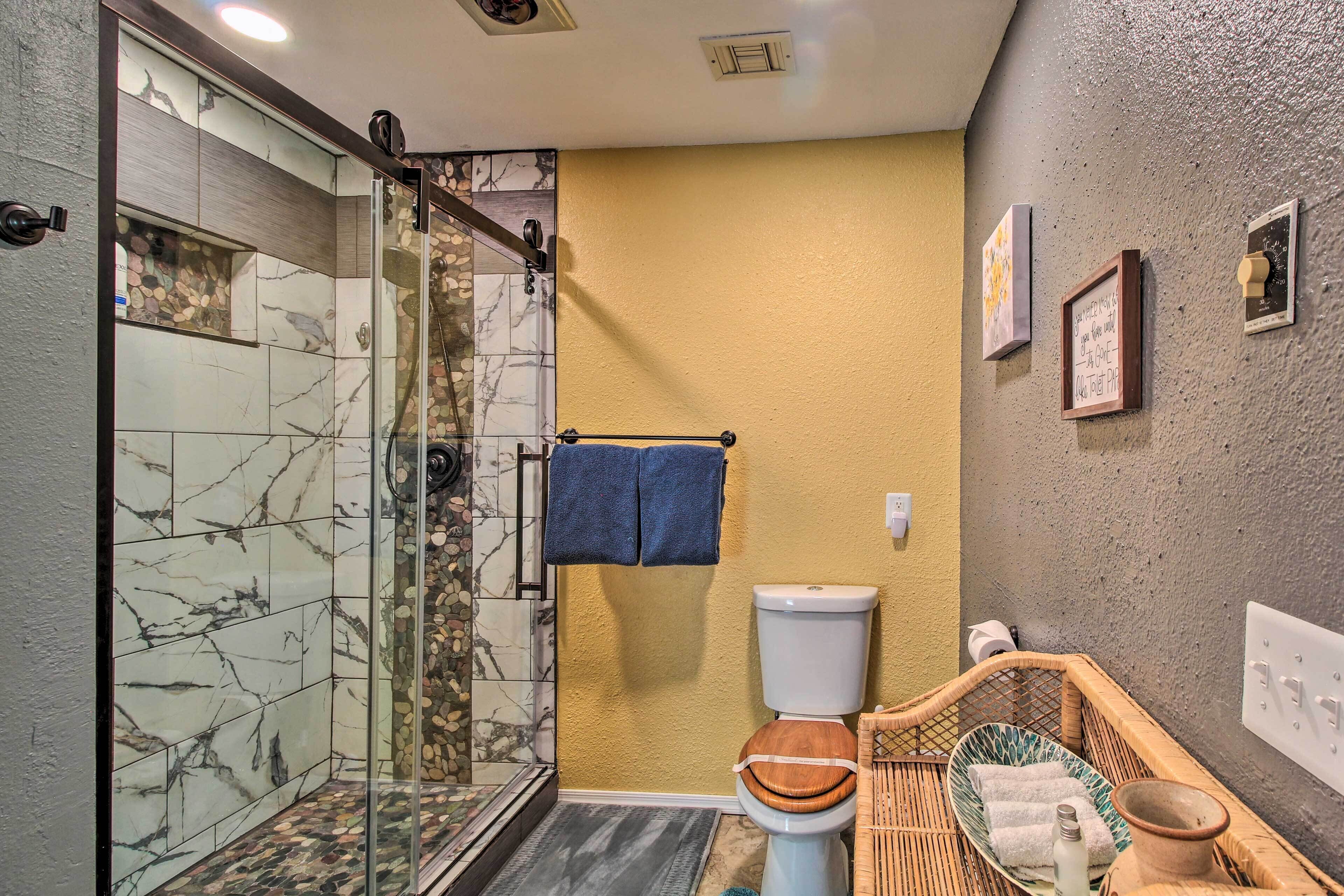 Un bagno con cabina doccia in vetro, uno scafo WC con seduta in legno e un cesto in vimini con asciugamani.