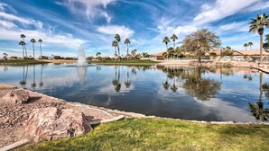A tranquil outdoor setting with a fountain, palm trees, and a clear blue sky. - Stunning Sun Lakes Home w/ Beautiful Lake Views! (Chandler)