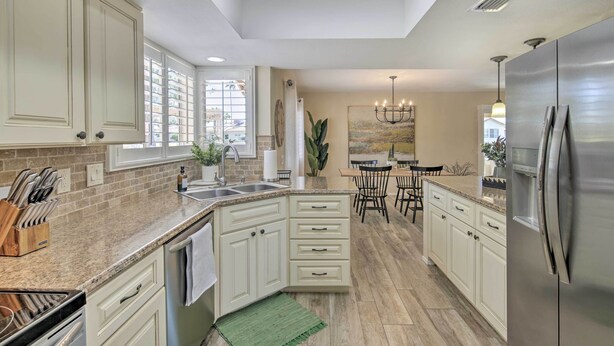 A kitchen with white cabinets, granite countertops, a stainless steel refrigerator, and a dining area with a chandelier. - Stunning Sun Lakes Home w/ Beautiful Lake Views! (Chandler)