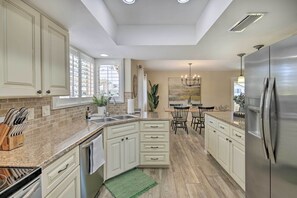 A kitchen with white cabinets, granite countertops, a stainless steel refrigerator, and a dining area with a chandelier.