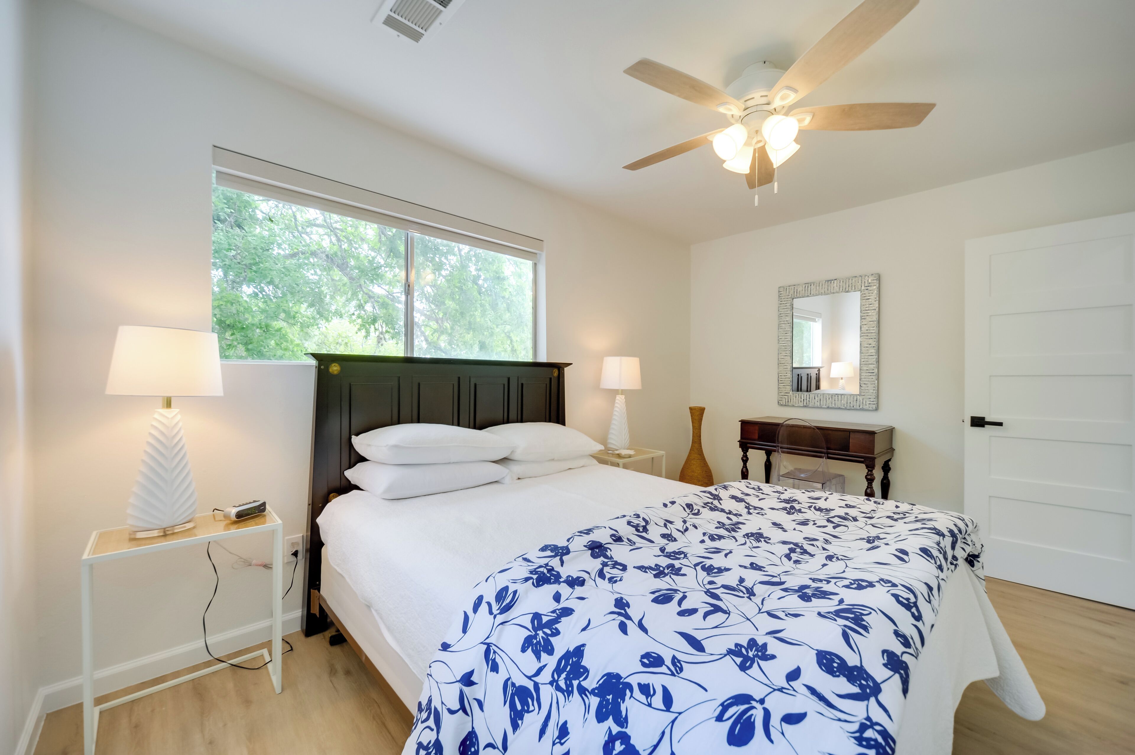 A bedroom with a bed, two bedside lamps, a nightstand, a ceiling fan, a window, and a door.