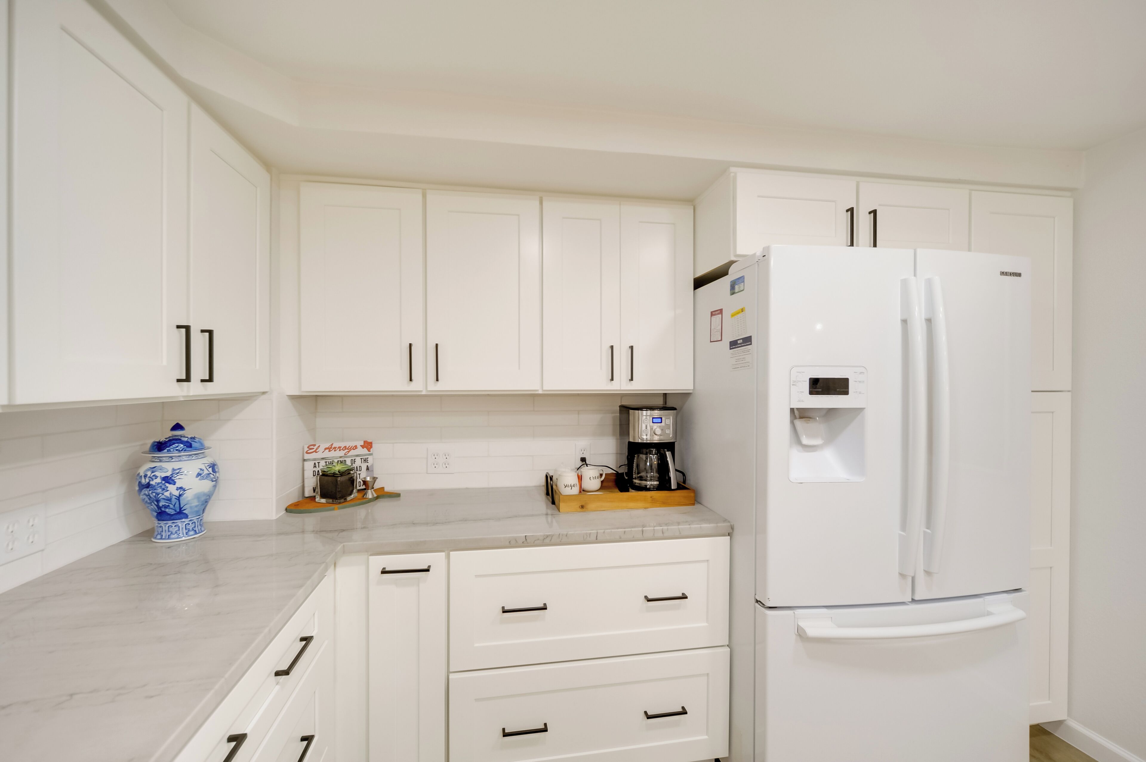 A modern kitchen with white cabinets, a white refrigerator, and a coffee maker on the countertop.