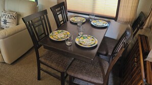 Un comedor con una mesa dispuesta para cuatro personas, rodeada de sillas, en una habitación con ventana y un sofá.