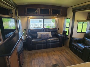 Interior acogedor de una caravana, con un sofá de cuero, una cafetera y una ventana con vistas al exterior.