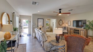 A spacious living room with a leather sofa, a round coffee table, and a television. There is a ceiling fan, a large mirror, and a clock on the wall. - Maricopa Retreat w/ Peaceful Backyard Oasis! (Maricopa)