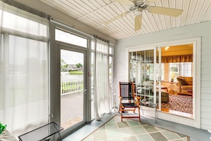 Una veranda con ampie porte scorrevoli in vetro, una ventola a soffitto e un angolo relax con una poltrona e un tavolino.