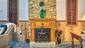 A stone fireplace with a star design, flanked by wooden shutters, and a green vase with flowers. - Charming Ingram Home w/ Yard & Furnished Patio! (Ingram)