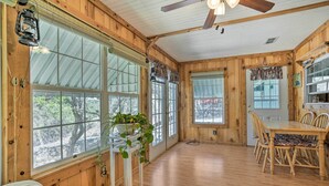 A wooden cabin interior with large windows, a dining table, chairs, and a ceiling fan. - Charming Ingram Home w/ Yard & Furnished Patio! (Ingram)