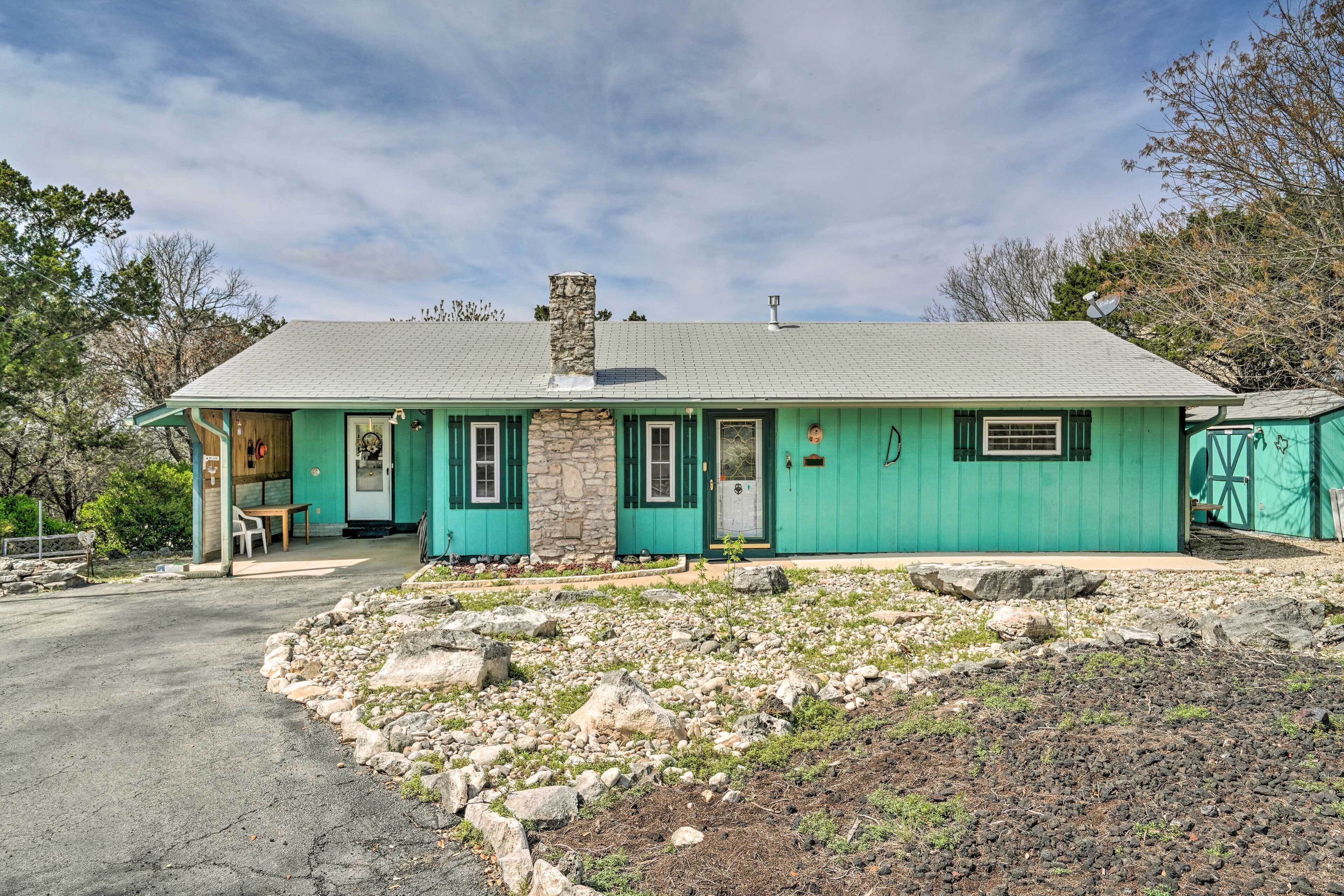 A single-story house with a stone chimney, green exterior, and a front porch with a table and chairs.