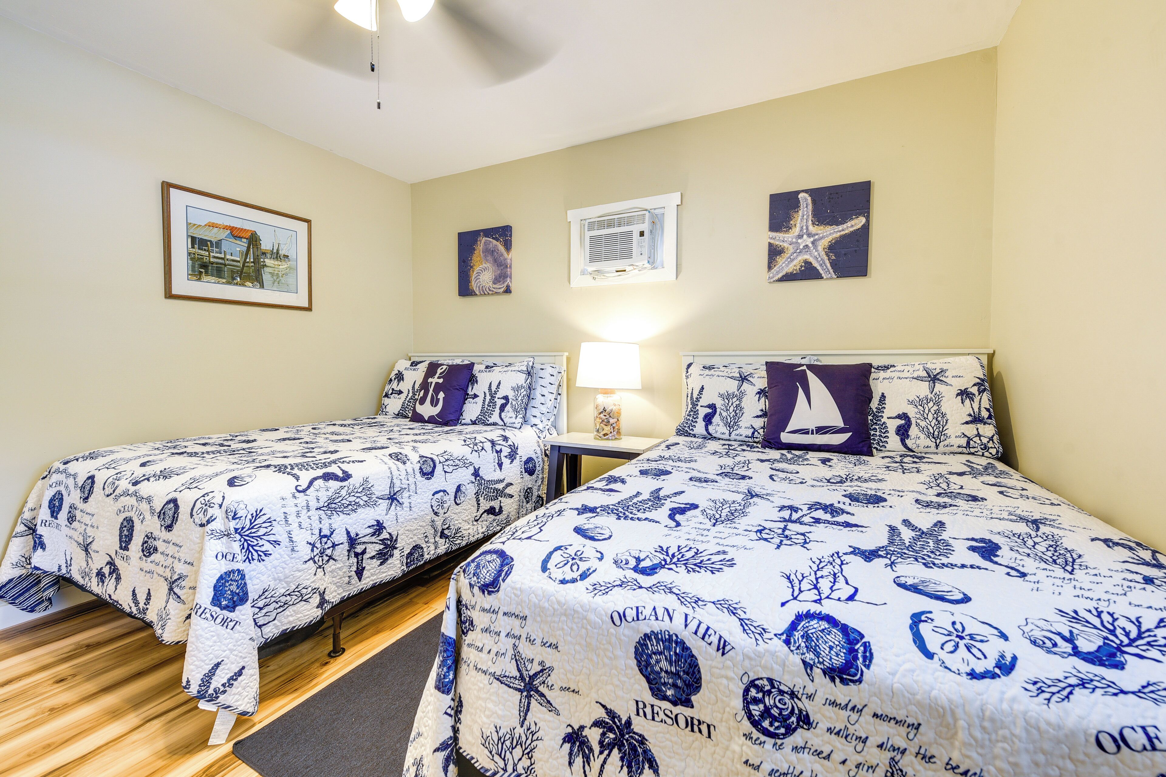 A room with two beds, a framed picture, an air conditioning unit, and a starfish decoration.