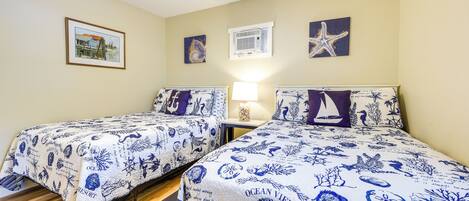 A room with two beds, a framed picture, an air conditioning unit, and a starfish decoration.