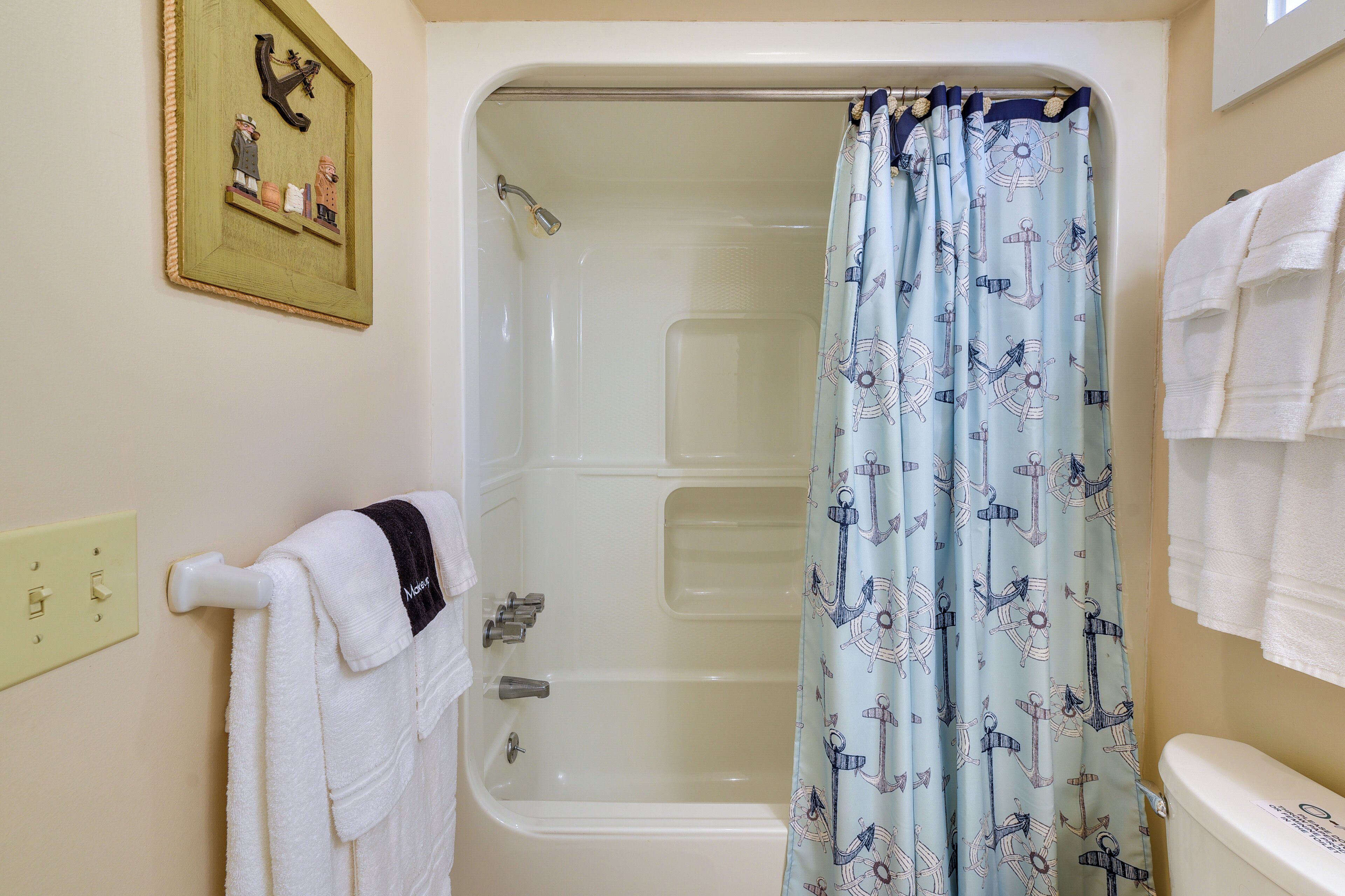 Un baño con bañera, cortina de ducha con motivos náuticos y toallero con toallas blancas.