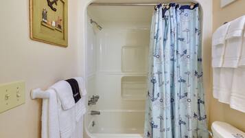 Un baño con bañera, cortina de ducha con motivos náuticos y toallero con toallas blancas.