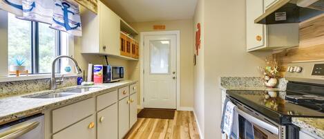 A kitchen with a microwave, toaster, and oven, wooden flooring, and a door with a doormat.