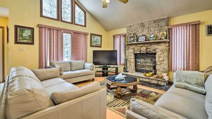 A living room with a stone fireplace, a flat-screen TV, and a large window. - Hot Tub + Deck: Pet-friendly Poconos Getaway! (Bushkill)