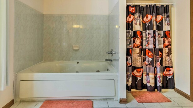 A bathroom with a large bathtub, a shower curtain with a cowboy theme, and two pink rugs on the floor. - Hot Tub + Deck: Pet-friendly Poconos Getaway! (Bushkill)