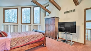Quarto com cama, televisão em móvel, armário e janelas amplas.