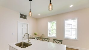A kitchen with a large island, white cabinets, a stainless steel sink, and pendant lights. There are two windows with shutters and a door with a vent above it. - Historic Madison Retreat - 1 Mi to Ohio River (Madison)