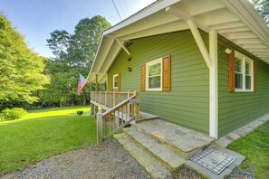 Uma casa verde com varanda, uma bandeira e um gramado bem cuidado.