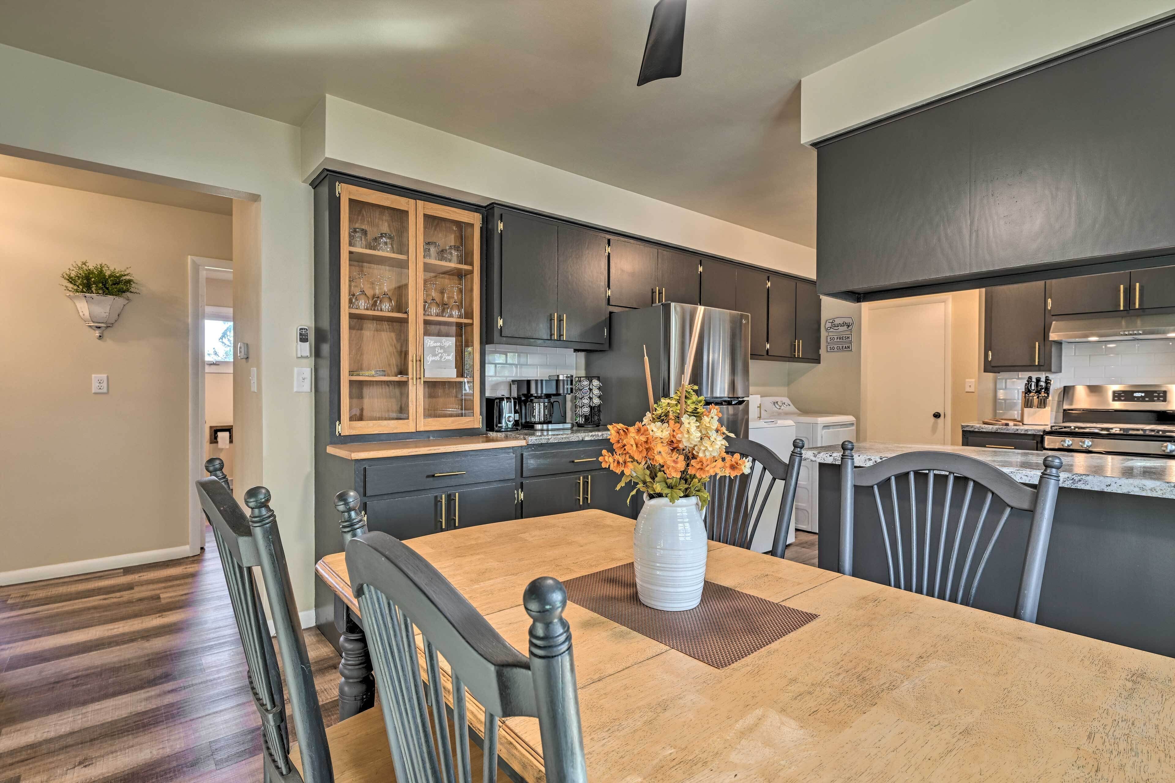 A modern kitchen with dark cabinetry, a central island, and a dining area with a wooden table and chairs.