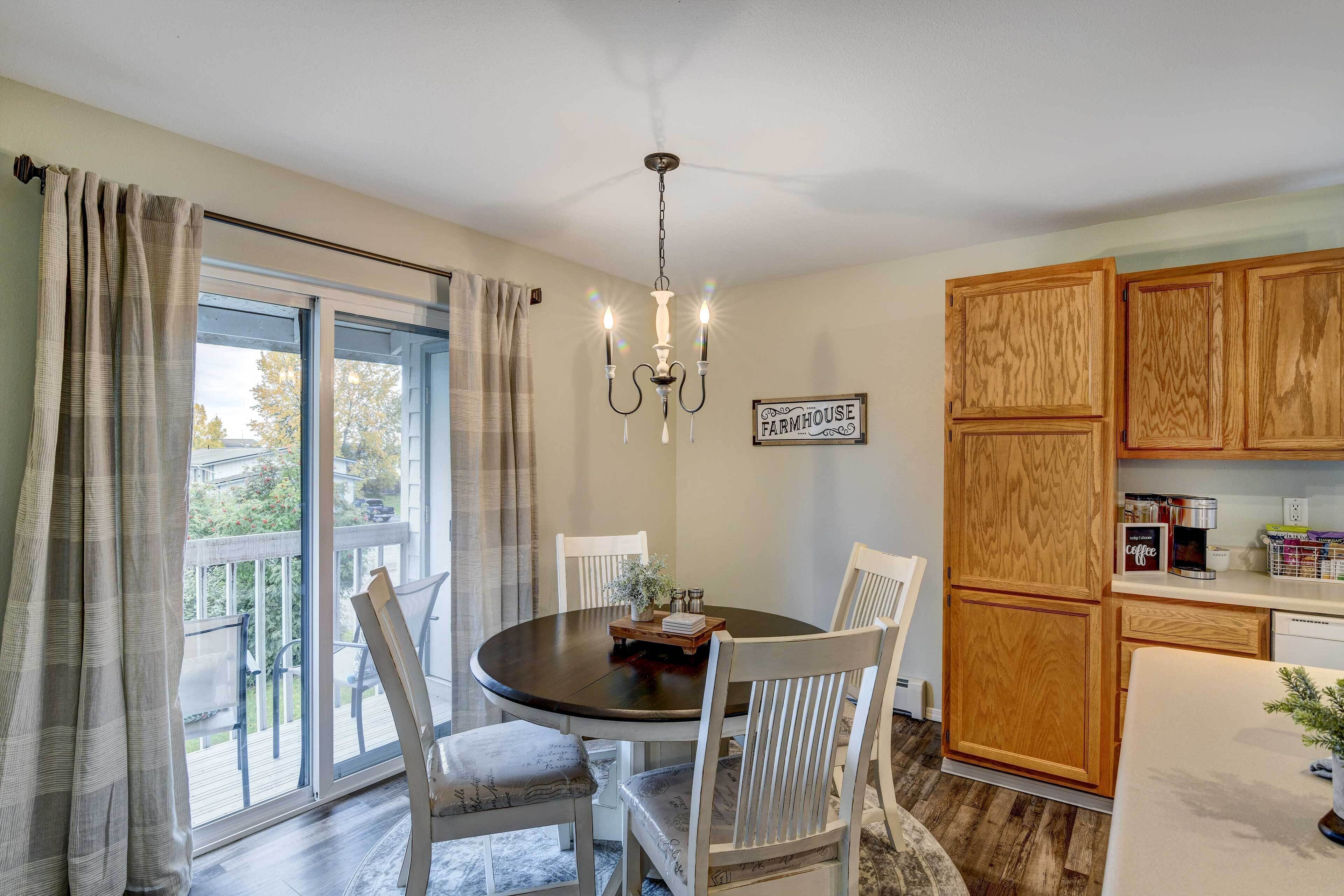 A dining area with a round table, white chairs, a chandelier, and a view of the outdoors through a sliding glass door.