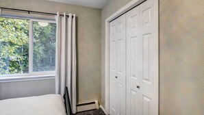 Quarto com uma cama, janela com cortinas, radiador e armário branco.