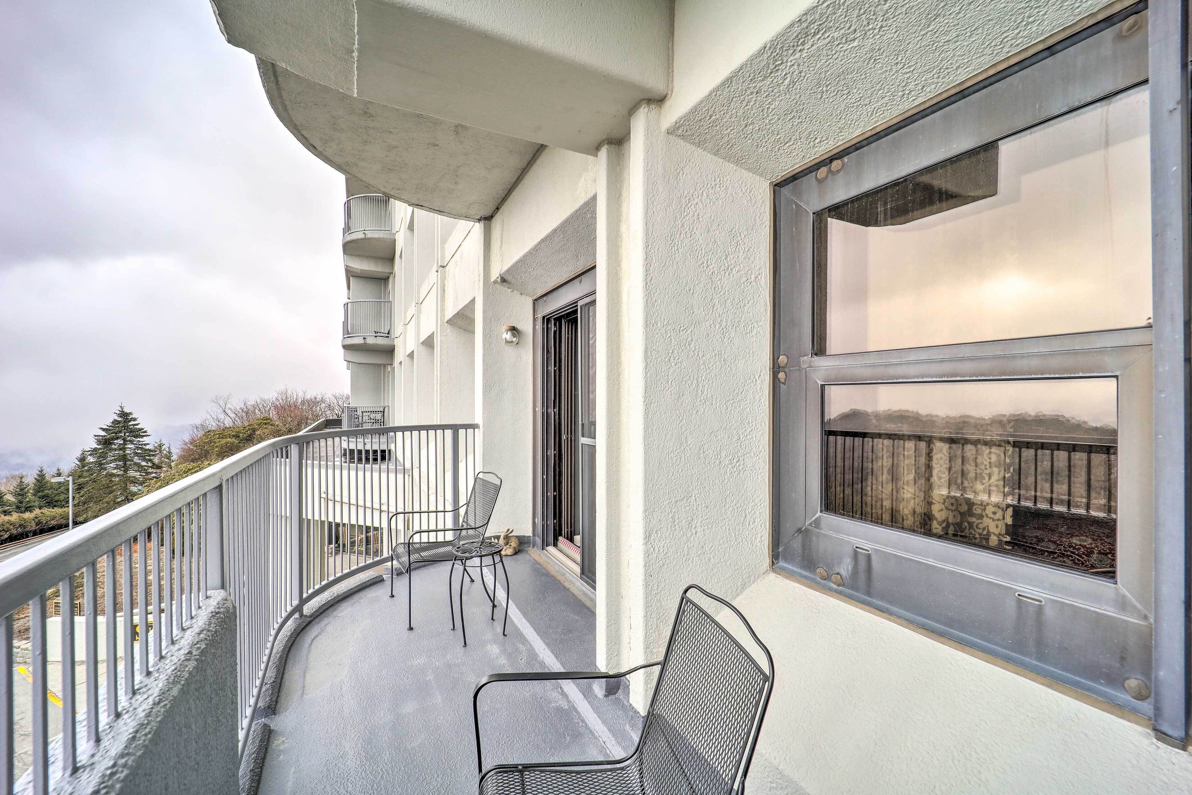 Un balcón con vistas al campo, una ventana con reja de metal y una silla.