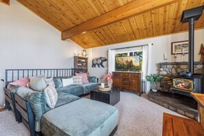 A cozy living room with a sofa, a fireplace, and a stone wall. - Hot Tub + Scenic Views: Luxury Twain Harte Cabin! (Twain Harte)