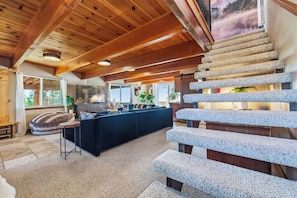 Interior moderno com escadaria de pedra, sofá escuro e televisão em um quarto com vigas de madeira.