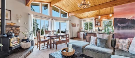 A cozy living room with a fireplace, a dining area, and a kitchen with large windows.