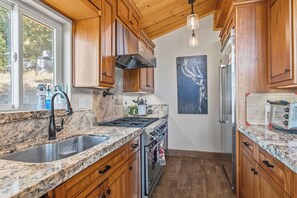 Una cocina con armarios de madera, estufa de acero inoxidable, un lavamanos y un refrigerador.