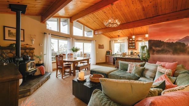 A cozy living room with a fireplace, wooden ceiling, and a large window overlooking a scenic view. - Hot Tub + Scenic Views: Luxury Twain Harte Cabin! (Twain Harte)