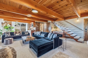 A spacious living area with a large black sectional sofa, a wooden ceiling, and a staircase with stone steps.