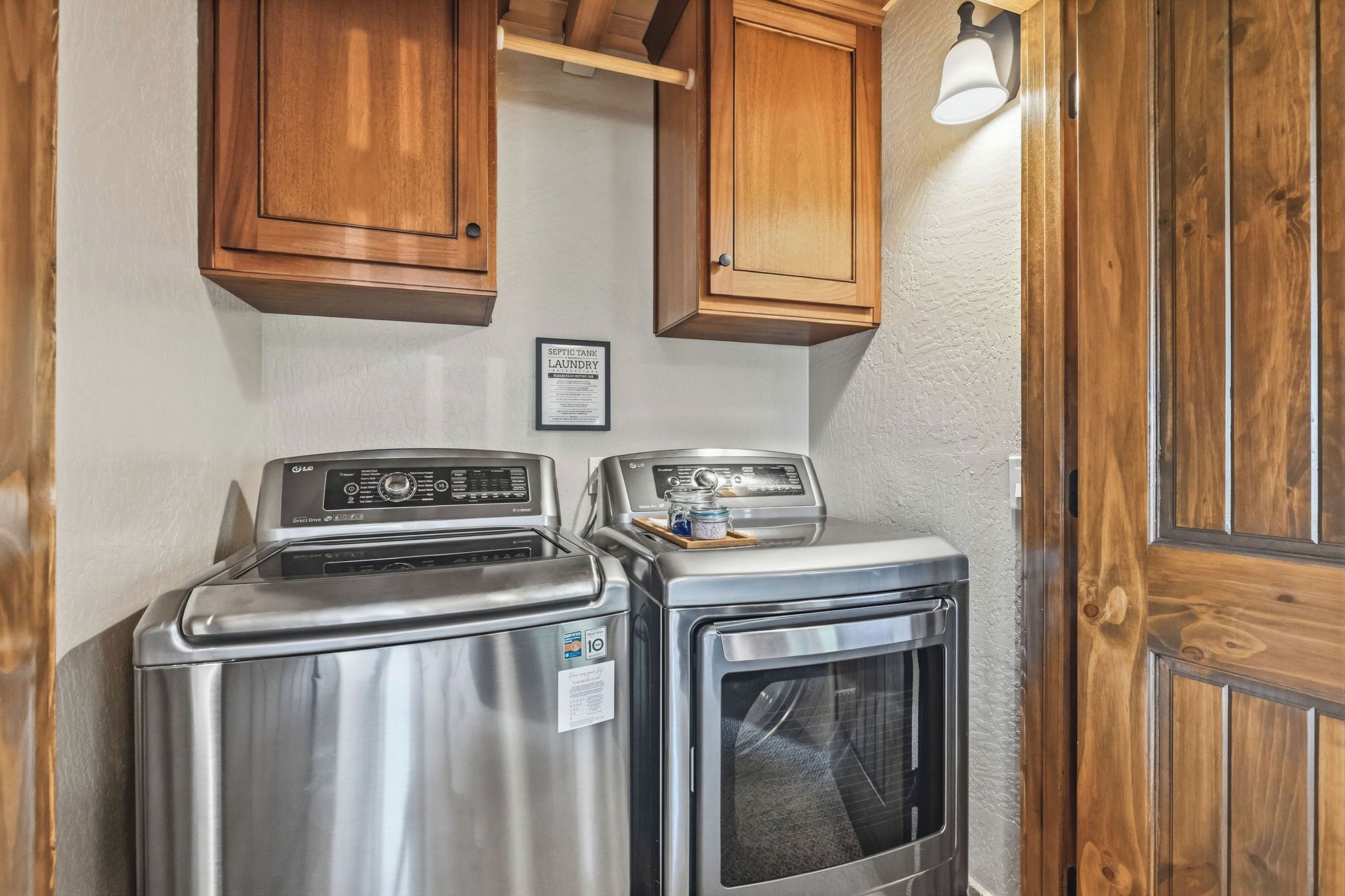 A compact laundry area with a washing machine and dryer, wooden cabinets, and a sign indicating a septic tank laundry facility.