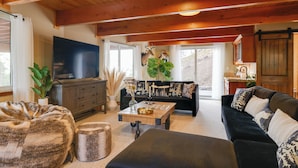 A spacious living room with a large flat-screen TV, a black sofa, a wooden coffee table, and a fireplace. - Hot Tub + Scenic Views: Luxury Twain Harte Cabin! (Twain Harte)