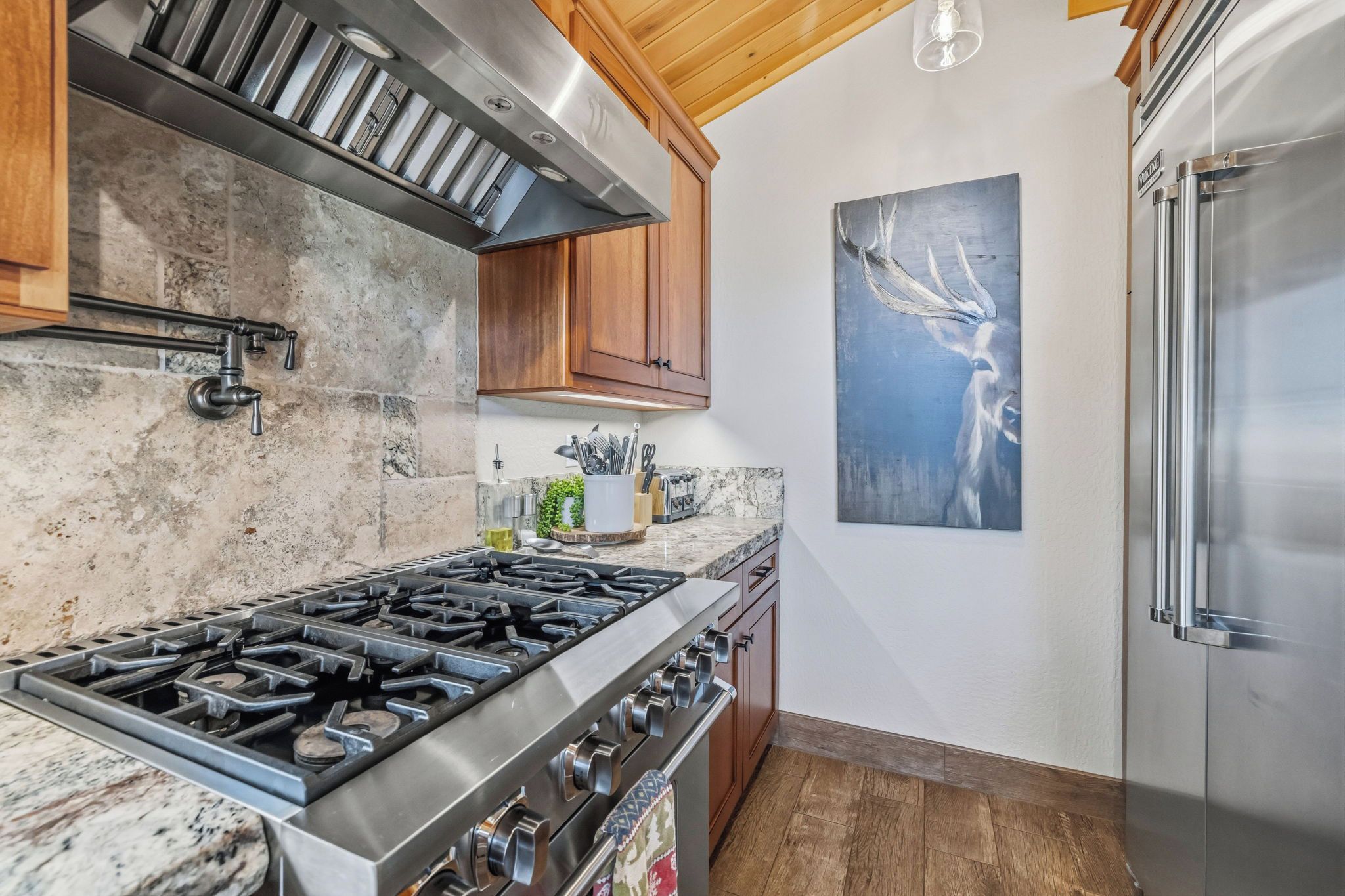A kitchen with a stainless steel stove, wooden cabinets, a marble countertop, and a modern refrigerator.