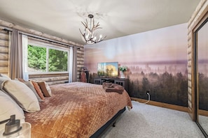 Un dormitorio con una cama grande, un televisor y un mural con un paisaje boscoso.