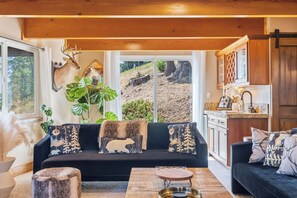 A cozy living room with a black sofa, a coffee table, and a dining area with a wooden table and chairs. - Hot Tub + Scenic Views: Luxury Twain Harte Cabin! (Twain Harte)