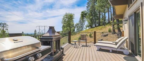 Eine Terrasse mit Grill, Gartenmöbeln und Blick auf den umliegenden Wald.