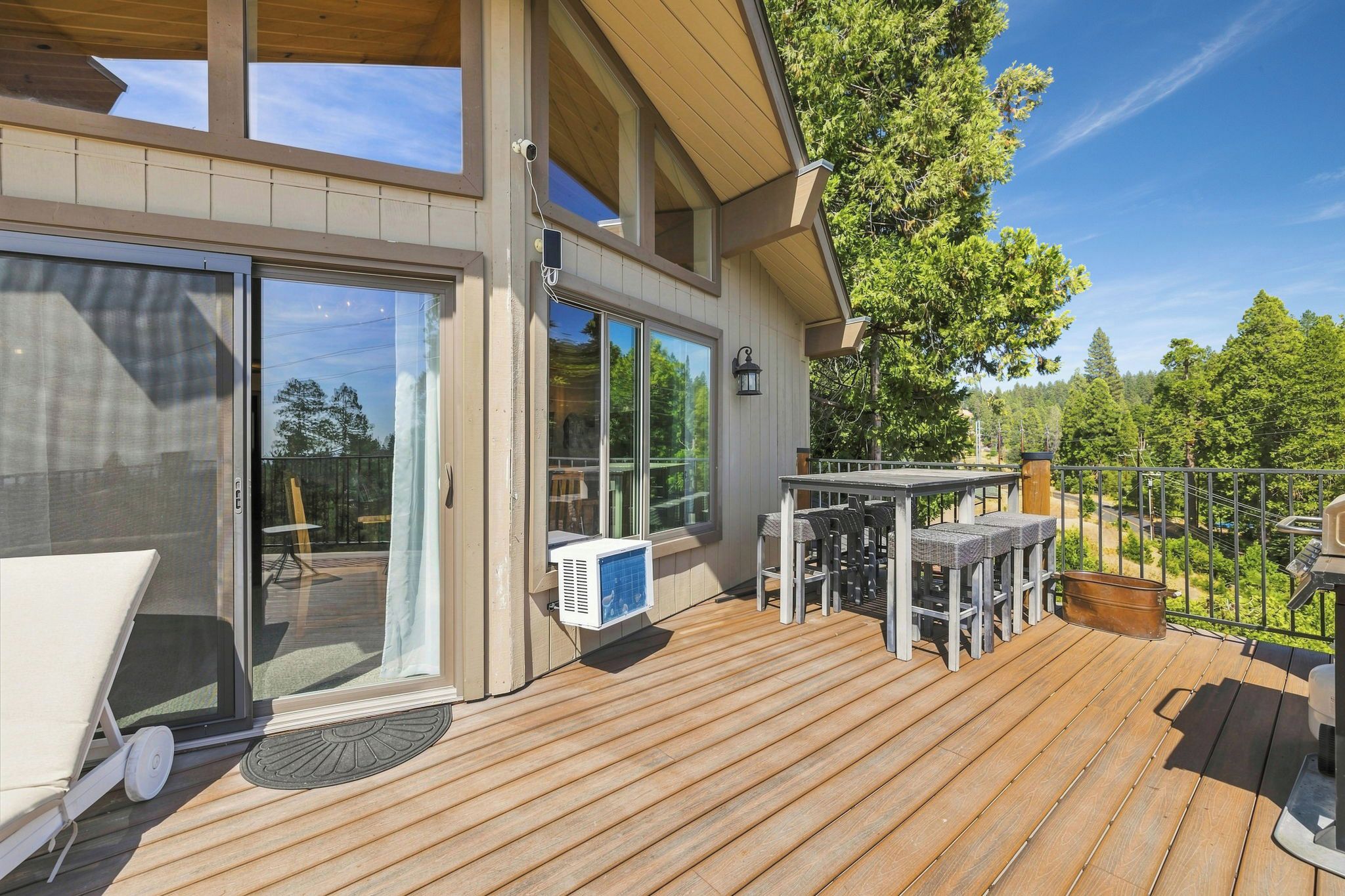 Una terraza de madera con mobiliario exterior, una puerta corrediza de vidrio y vistas a los árboles circundantes.