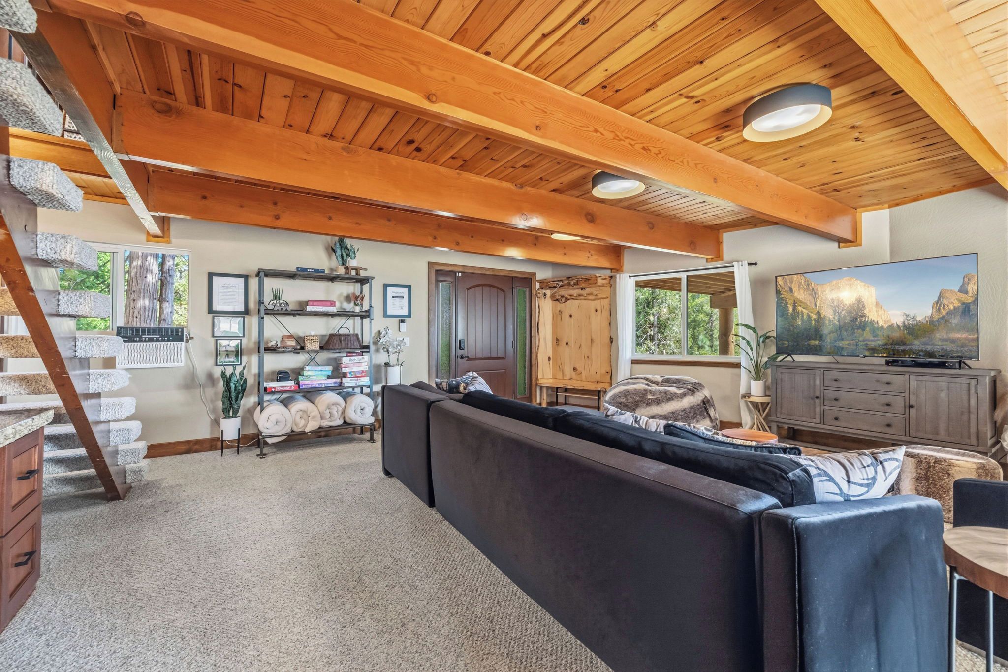 A cozy living room with a large sofa, a wooden ceiling, a bookshelf, and a television.